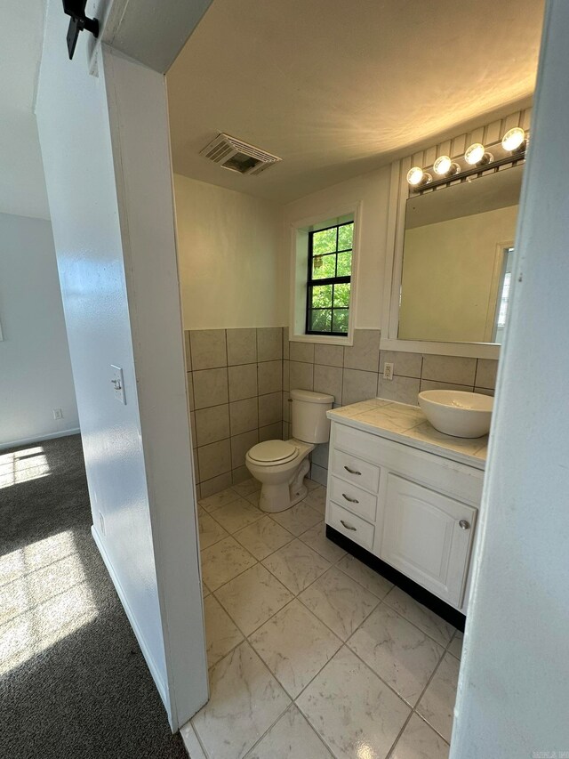 bathroom with toilet, vanity, and tile walls