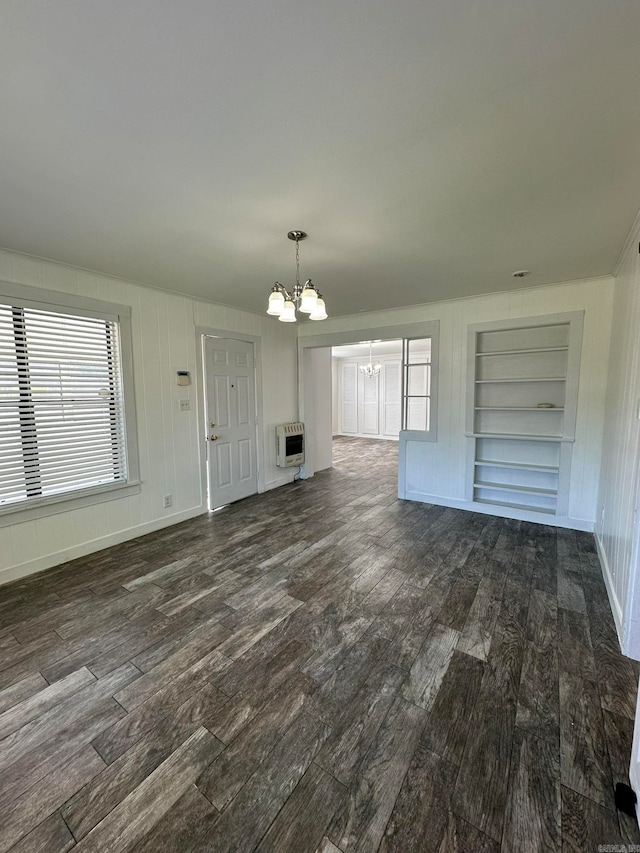 unfurnished living room with built in shelves, dark wood-type flooring, a chandelier, and heating unit