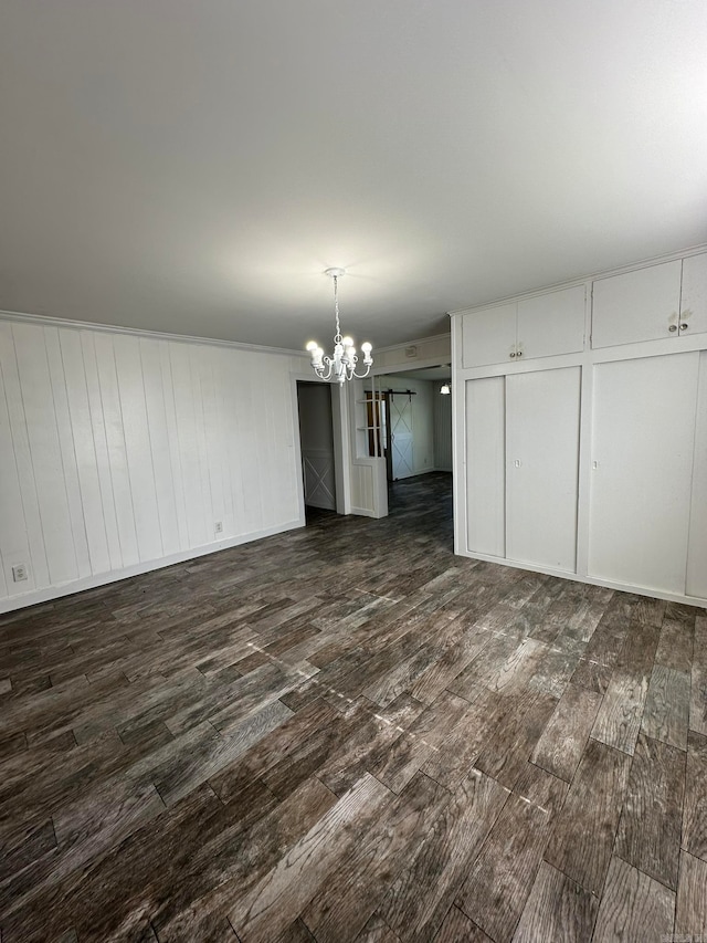 unfurnished dining area featuring dark wood-type flooring, a chandelier, and a barn door