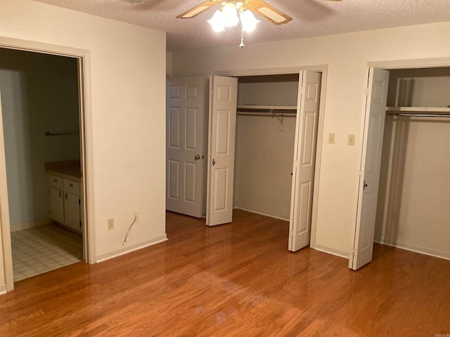 unfurnished bedroom with ensuite bath, light wood-type flooring, a textured ceiling, multiple closets, and ceiling fan