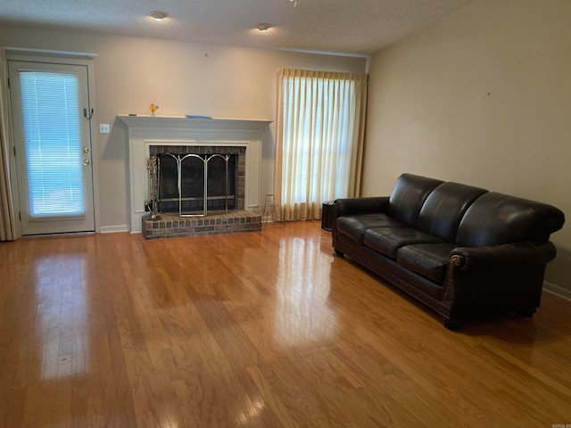 living room featuring a brick fireplace, a textured ceiling, and hardwood / wood-style floors