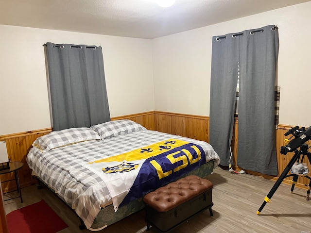 bedroom featuring a wainscoted wall, light wood-style floors, and wood walls