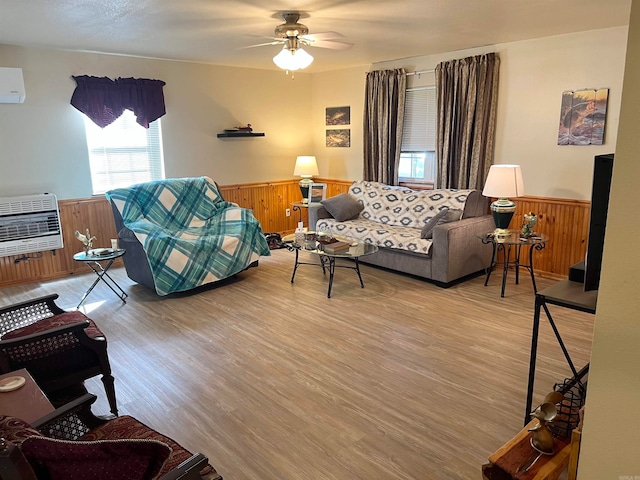 living area featuring light wood finished floors, ceiling fan, a wainscoted wall, an AC wall unit, and heating unit