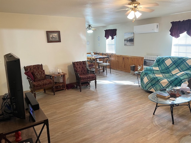 living area with a wall mounted air conditioner, light wood-style floors, a healthy amount of sunlight, and ceiling fan