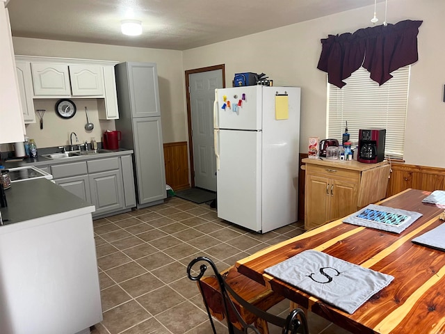 kitchen featuring a wainscoted wall, dark tile patterned flooring, freestanding refrigerator, a sink, and white cabinetry