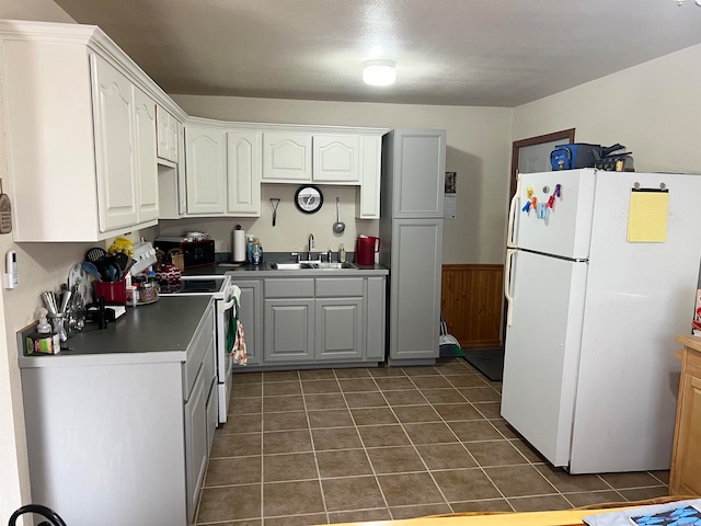 kitchen featuring dark tile patterned floors, wainscoting, white appliances, white cabinetry, and a sink