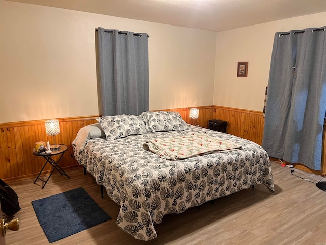 bedroom featuring wooden walls, wood finished floors, and wainscoting