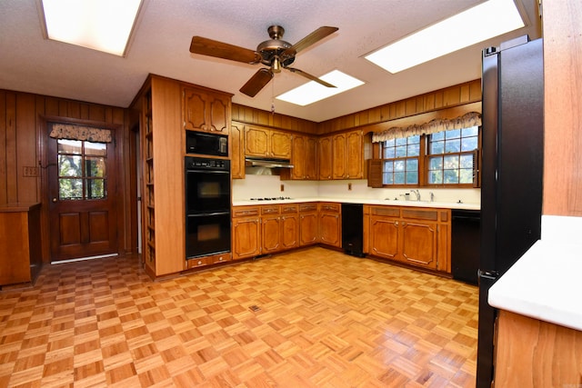 kitchen featuring black appliances, light parquet floors, a textured ceiling, wooden walls, and ceiling fan