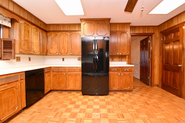 kitchen with wood walls, black appliances, light parquet flooring, and a skylight