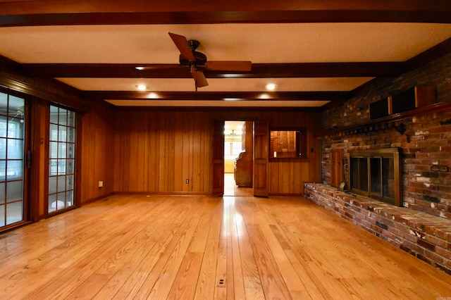 unfurnished living room with a fireplace, light wood-type flooring, wood walls, beamed ceiling, and ceiling fan