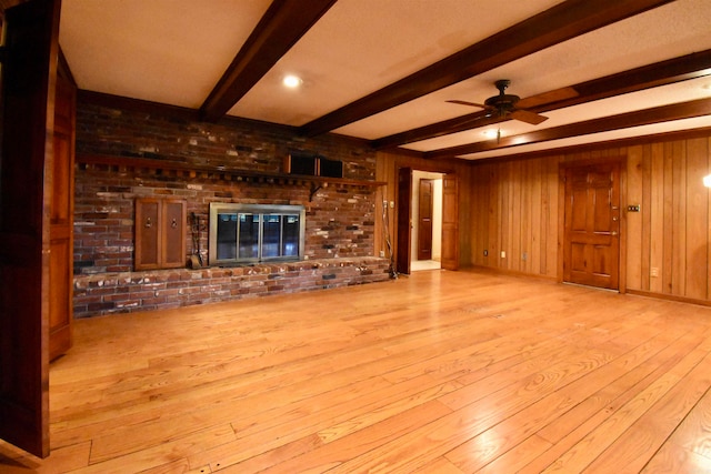 unfurnished living room with light hardwood / wood-style flooring, wooden walls, beamed ceiling, and ceiling fan