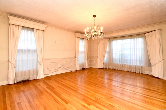 spare room featuring ornamental molding, wood-type flooring, a notable chandelier, and a healthy amount of sunlight