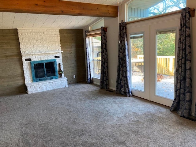 unfurnished living room with carpet flooring, a fireplace, lofted ceiling with beams, and wooden walls