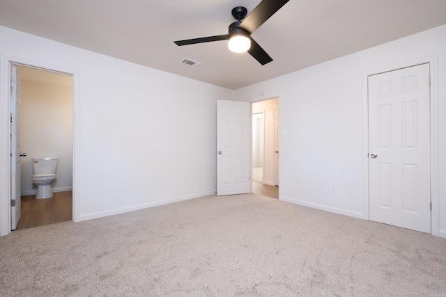 unfurnished bedroom featuring ensuite bathroom, light colored carpet, and ceiling fan