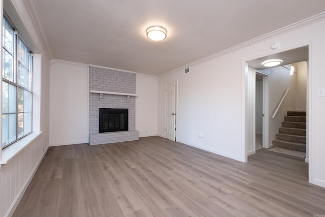 unfurnished living room featuring a brick fireplace, light wood-type flooring, and crown molding