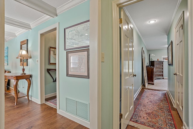 corridor with beamed ceiling, hardwood / wood-style floors, ornamental molding, and a textured ceiling