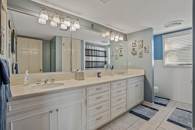 bathroom with tile walls, tile patterned flooring, vanity, and a textured ceiling