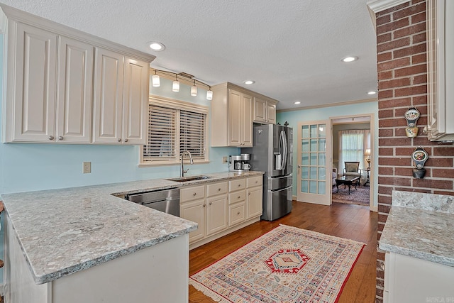 kitchen with ornamental molding, appliances with stainless steel finishes, light stone countertops, sink, and hardwood / wood-style flooring