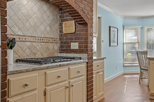 kitchen featuring light stone counters, ornamental molding, light tile patterned flooring, stainless steel gas cooktop, and cream cabinetry