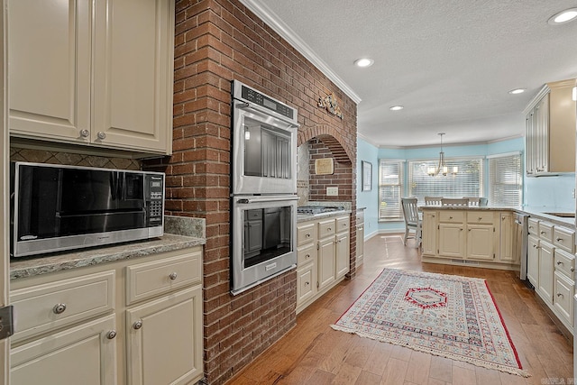 kitchen featuring crown molding, appliances with stainless steel finishes, hanging light fixtures, an inviting chandelier, and light hardwood / wood-style floors