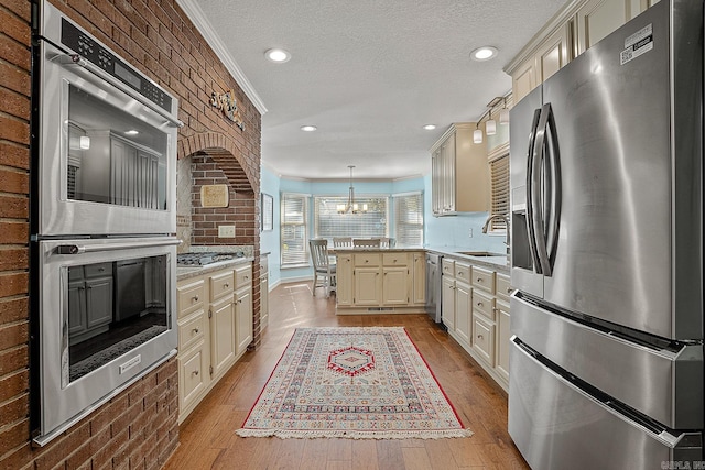 kitchen featuring stainless steel appliances, cream cabinetry, decorative light fixtures, and light wood-type flooring