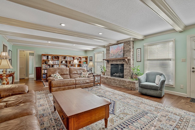 living room with crown molding, a textured ceiling, beam ceiling, a brick fireplace, and light hardwood / wood-style flooring