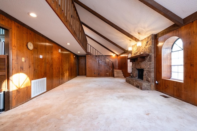 unfurnished living room featuring a stone fireplace, wood walls, a textured ceiling, and lofted ceiling with beams