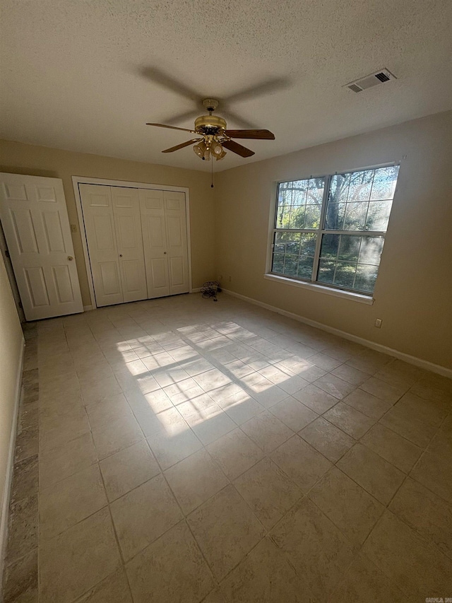 unfurnished bedroom featuring light tile patterned flooring, ceiling fan, a textured ceiling, and a closet