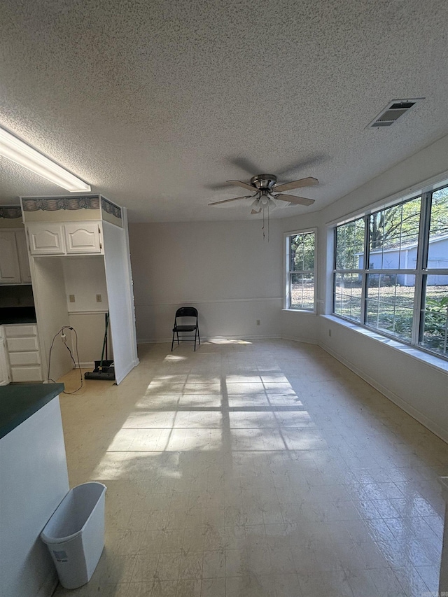 unfurnished living room featuring ceiling fan, a textured ceiling, and baseboards