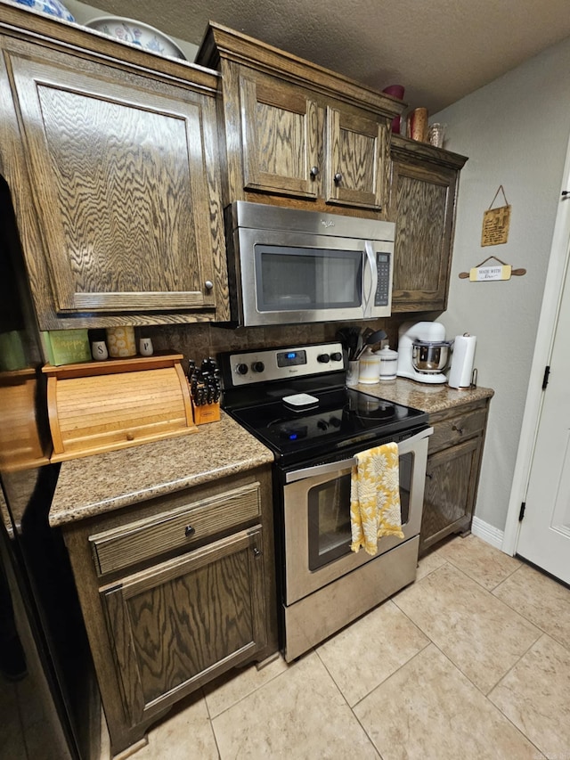 kitchen with dark brown cabinets, appliances with stainless steel finishes, a textured ceiling, and light tile patterned flooring