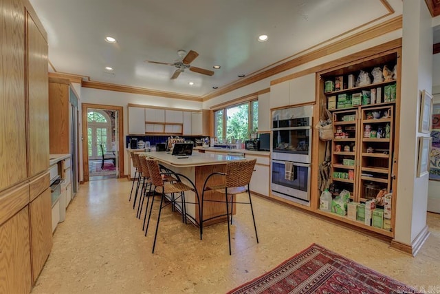 kitchen with stainless steel double oven, crown molding, white cabinetry, a kitchen breakfast bar, and a center island