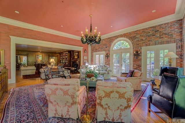 living room featuring french doors, ornamental molding, light wood-type flooring, a chandelier, and brick wall