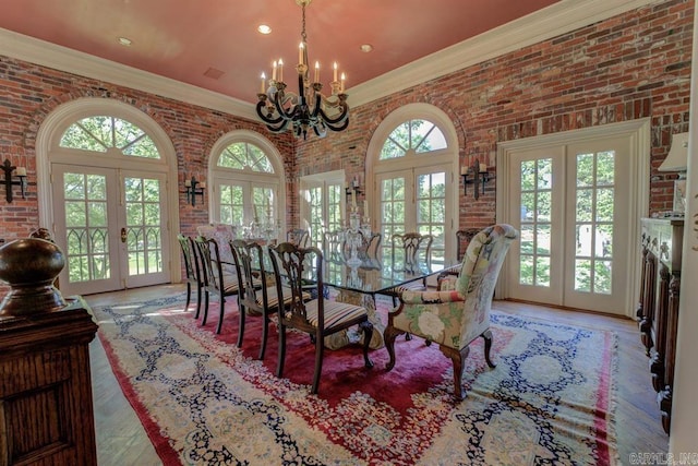 dining space with a chandelier, crown molding, brick wall, and french doors