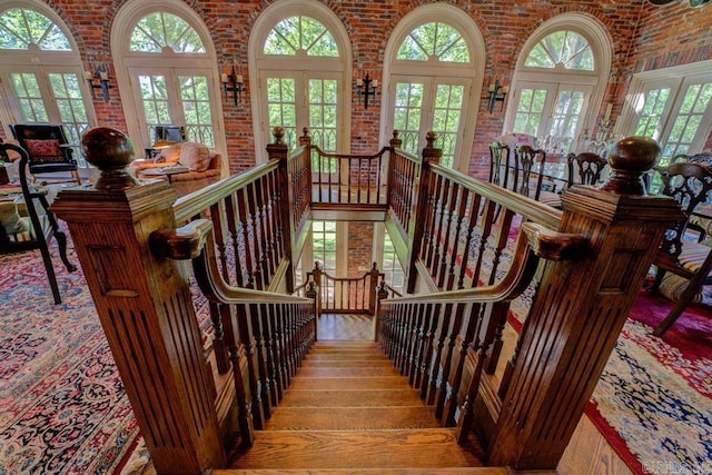 stairway featuring a high ceiling, wood-type flooring, french doors, and brick wall