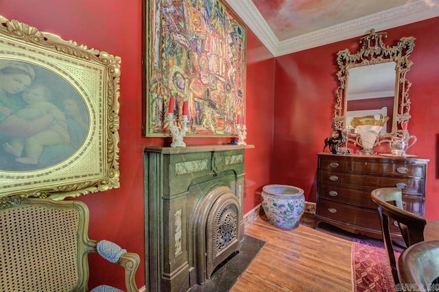 sitting room with wood-type flooring, a stone fireplace, and ornamental molding