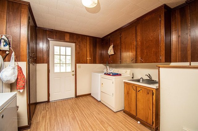 clothes washing area featuring light hardwood / wood-style floors, cabinets, wood walls, sink, and independent washer and dryer