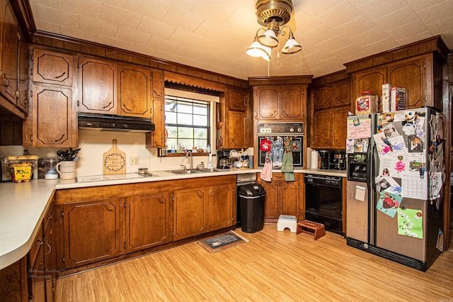 kitchen featuring hanging light fixtures, light wood-type flooring, black appliances, and sink