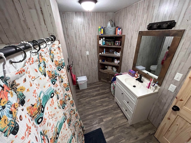 bathroom with wood walls, a textured ceiling, wood-type flooring, vanity, and toilet