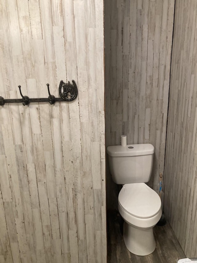 bathroom with toilet, wood walls, and wood-type flooring