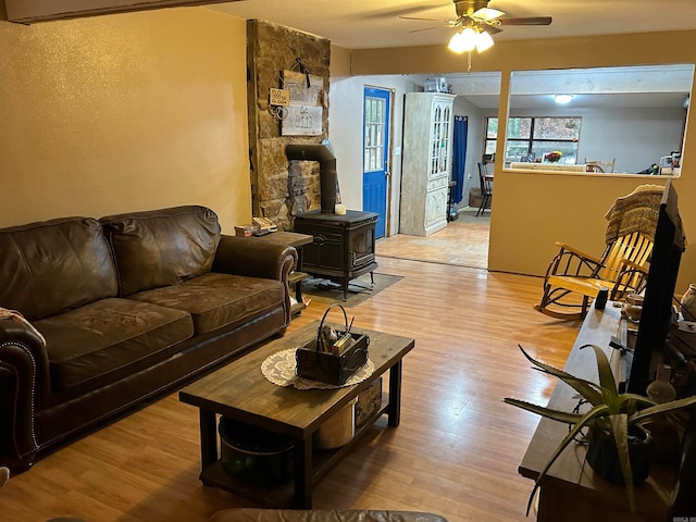 living room with light wood-type flooring, a wood stove, and ceiling fan