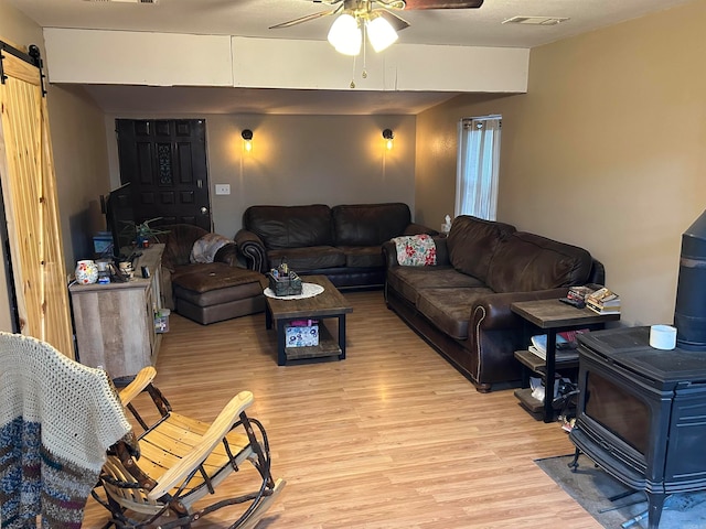 living room featuring light wood-type flooring, a barn door, ceiling fan, and a wood stove