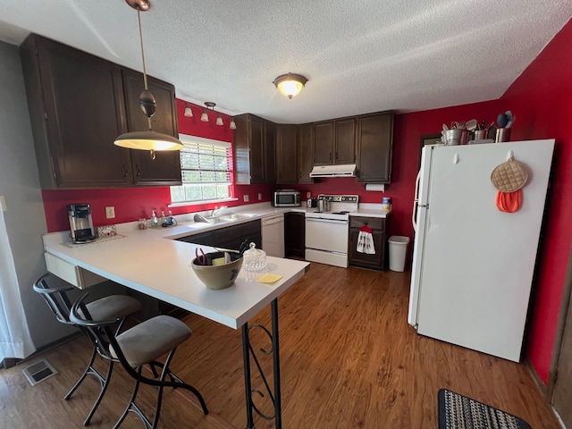 kitchen with decorative light fixtures, kitchen peninsula, a textured ceiling, light wood-type flooring, and white appliances