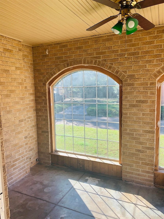 interior space with concrete flooring, ceiling fan, and brick wall