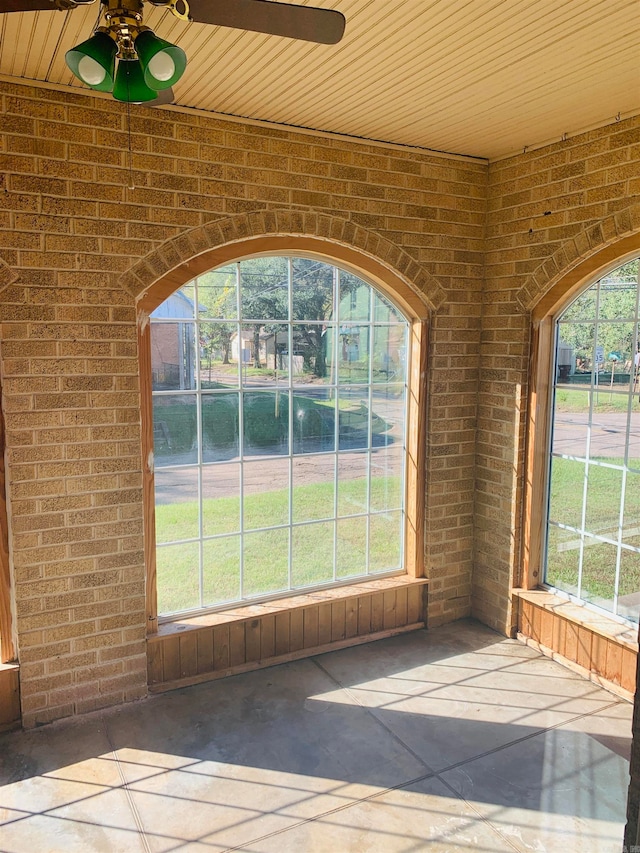 unfurnished sunroom featuring wooden ceiling, ceiling fan, and a healthy amount of sunlight