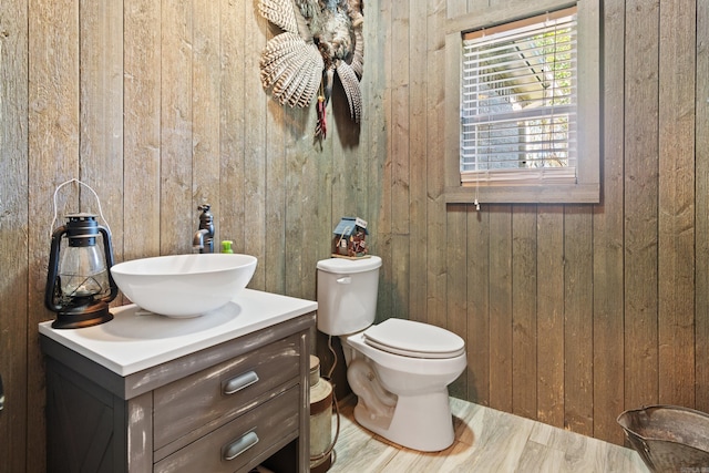 bathroom featuring vanity, hardwood / wood-style flooring, wooden walls, and toilet