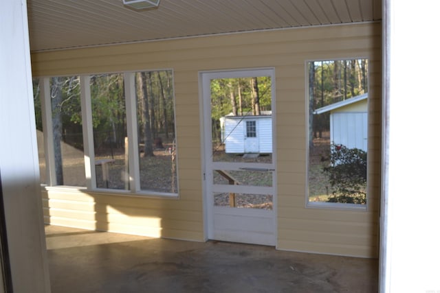 doorway to outside featuring concrete flooring, wooden walls, and plenty of natural light