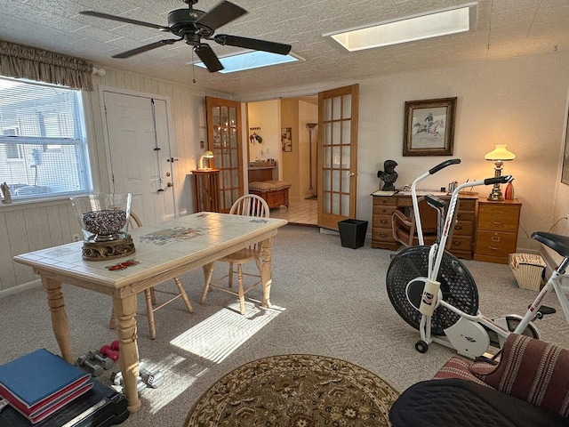 carpeted office space featuring wooden walls, french doors, ceiling fan, and a textured ceiling