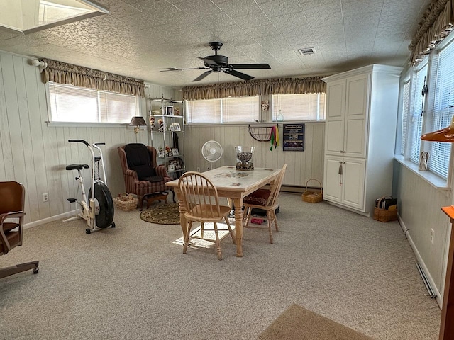 dining space with carpet, wooden walls, and ceiling fan