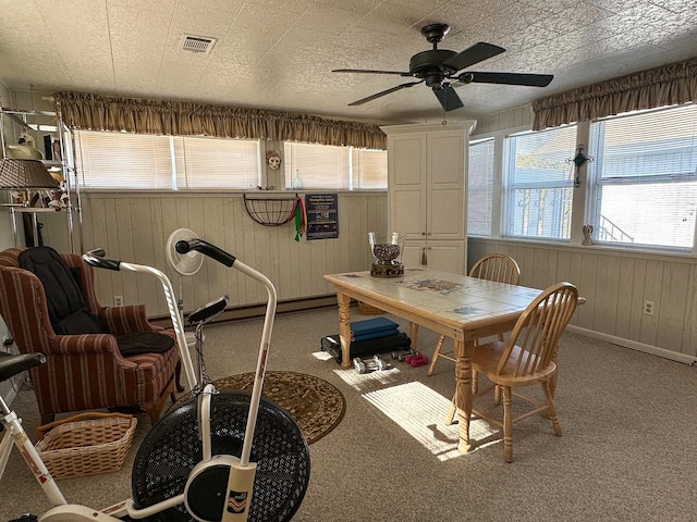 dining area featuring a textured ceiling, carpet, wood walls, and ceiling fan