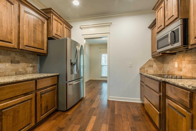 kitchen with appliances with stainless steel finishes, dark hardwood / wood-style flooring, tasteful backsplash, light stone counters, and crown molding